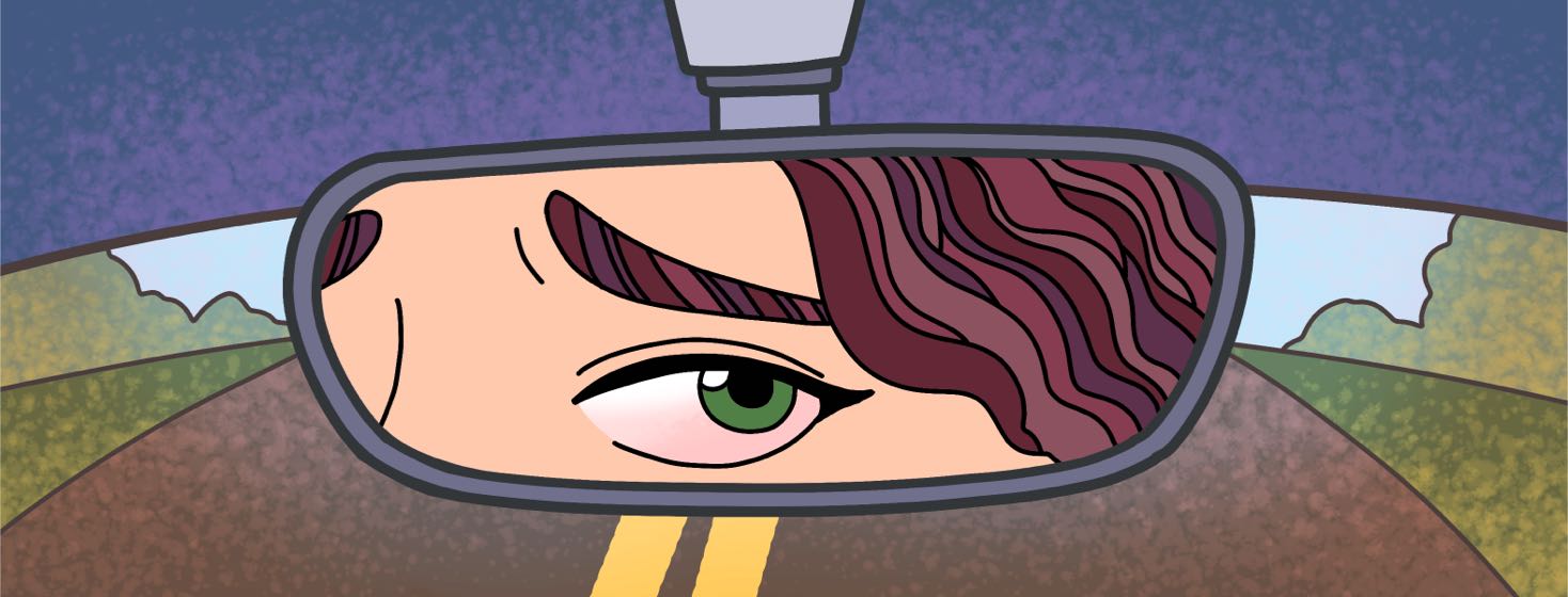A person's red, irritated eye looks in the rearview mirror while driving down a road.